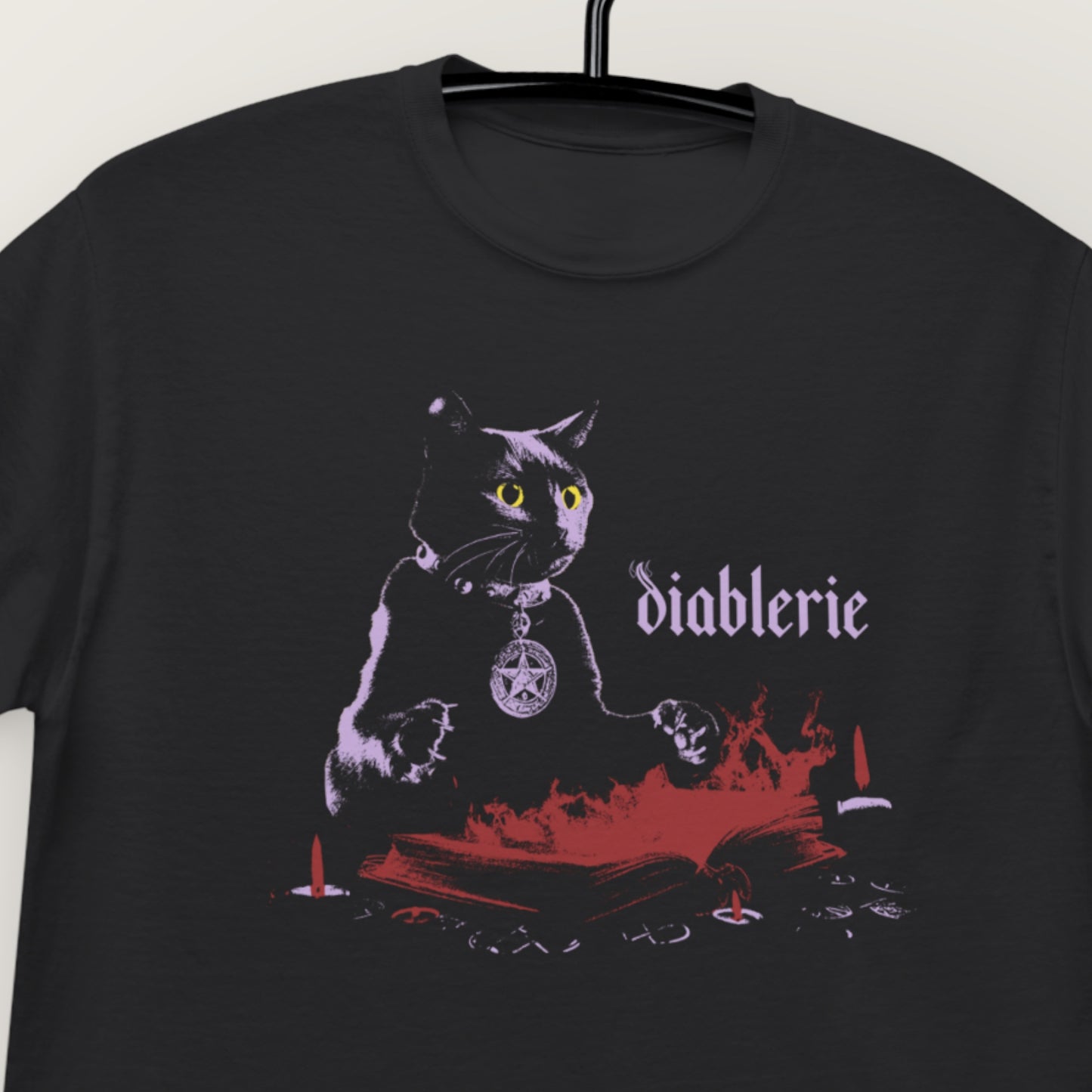Dark Arts black cat spellbook t-shirt hanging on a hanger, close-up of the chest print and Diablerie logo.
