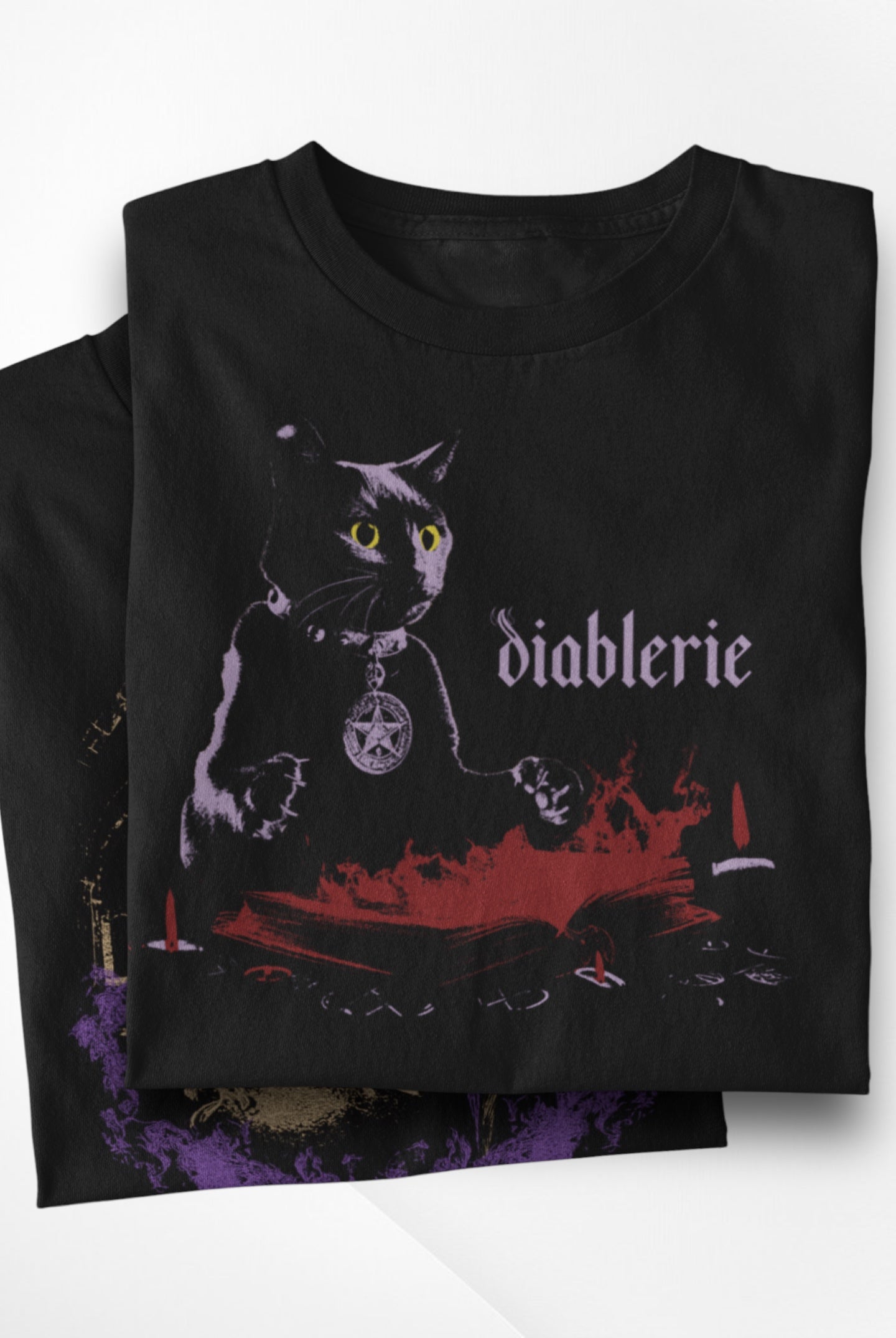 Stack of folded Dark Arts black cat graphic t-shirts, with the top shirt showing the cat, spellbook, and flames design.